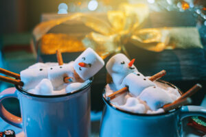 a mug with hot chocolate on a wooden table with a marshmallow man who is resting in a mug
