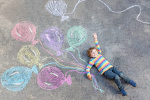 Cute little kid boy playing and flying with colorful balloons picture drawing with chalk. Creative leisure for children outdoors in summer, celebrating birthday
