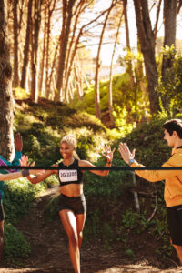 Happy marathon runner being greeted by group of supporter at finish line in the race. African woman finishing marathon race in forest.