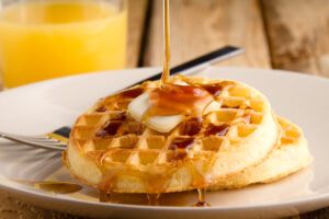 This s a photo of a couple waffles being soaked in syrup. Shot on a wooden table with a shallow depth of field.