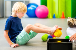 Child during physical therapy session. Boy exercising barefoot with textured surface ball in physio therapy. Flat feet.