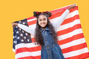 Cheerful delighted girl smiling to you while holding up a US flag