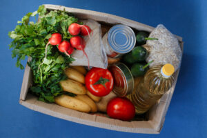Donation box with food on a blue background. Fruits, vegetables, canned food, pasta and sunflower oil in a box. Social assistance with food.