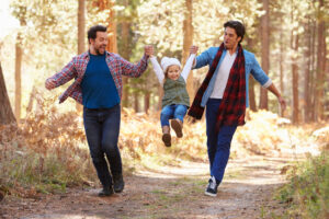 Couple With Daughter Walking Through Fall Woodland