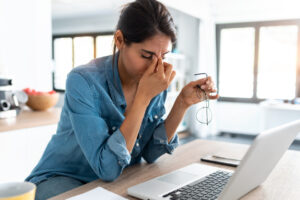 woman working from home on laptop looking worried, tired and overwhelmed.