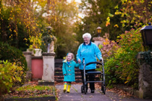 Happy senior lady with a walker or wheel chair and children. Grandmother and kids enjoying a walk in the park. Child supporting disabled grandparent. Family visit. Generations love and relationship.