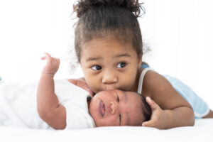 little girl kissing on newborn baby cheek on white bed at home.