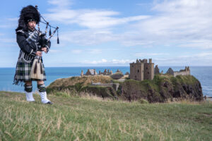 Traditional scottish bagpiper in full dress code at Dunnottar Castle