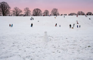 "Snowman in forground has his back to the action with Late Afternoon Family Fun in the snow against a stunning sky. Taken on Hexham Sele, Northumberland, England"