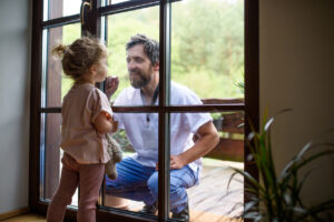 Doctor coming to see and greet family in isolation, window glass separating them.