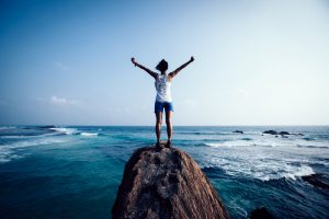 young woman outstretched arms on seaside rock cliff edge