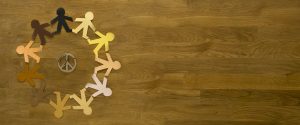 Paper dummies of different skin colors joined together around peace symbol