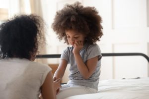 Caring african mother holds hand of sad little daughter talks gives support consoling kid, small mixed-race girl seated on bed touch cheek suffers from toothache, share mental or physical pain concept
