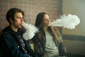 Vape teenagers. Young cute girl in sunglasses and young handsome guy smoke an electronic cigarettes in the vape bar. Bad habit that is harmful to health. Vaping activity.