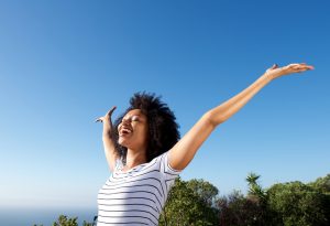 Portrait of young african woman standing outdoors with arms raised and laughing