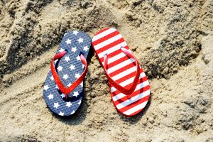 Pair of flip-flops with USA flag pattern placed on sand