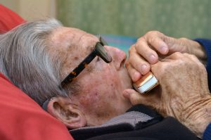Old man plays a harmonica in bed. Concept photo of old age, lonely, alone, retirement, music, sad.