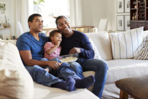 Three generation family male family group sitting on a sofa in the living room eating popcorn and watching TV, selective focus