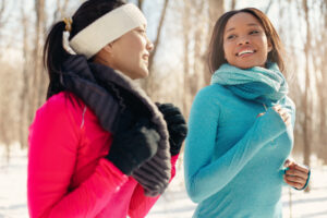 Diverse duo of millenial young adult friends take a break while training for cross-country running in the wintertime in a snow-filled park