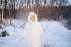 Happy elderly senior mature woman in white warm outwear playing with snow in sunny winter outdoors. Retired healthy people holiday vacation winter activities, active lifestyle concept