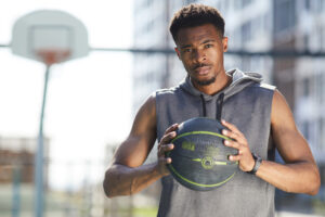Waist up portrait of muscular African man holding basketball ball in outdoor court and looking at camera, copy space