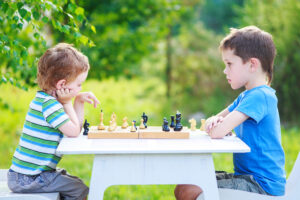 older brother and younger brother sitting opposite each other and playing chess