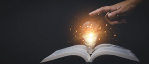 Thinking and creative concept, Hand touch Light bulb on the Book and light bulb style bokeh vintage dark background,Concept The idea of reading books, knowledge, and searching for new ideas.