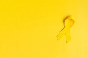 Yellow Ribbon on yellow background for supporting people living and illness. July Sarcoma cancer, Suicide prevention day, Childhood Cancer Awareness month concept