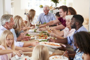 Group Of Multi-Generation Family And Friends Sitting Around Table And Enjoying Meal