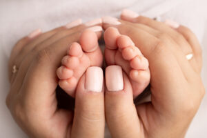 Mother is doing massage on her baby foot. Closeup baby feet in mother hands. Prevention of flat feet, development, muscle tone, dysplasia. Family, love, care, and health concepts. Studio macro.