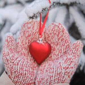 Woman hand decorates christmas tree with heart shaped balls in winter nature on new year's eve