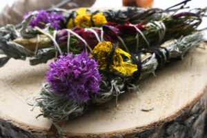 A close up image of three handmade healing smudge sticks on a wood cookie.