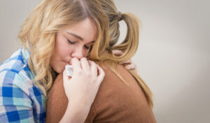 Closeup on sad teen daughter crying by problems in the shoulder of her mother. Mother embracing and consoling daughter.