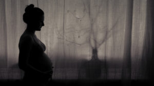 xPregnant woman stands in the light of a night window