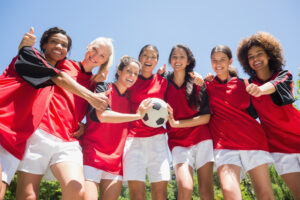 Portrait of successful female soccer players gesturing thumbs up against clear blue sky