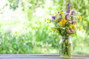 Wildflowers in glass jar stand on wooden table in the garden. Summer rural scene. Copy space.