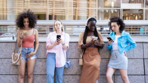 Four girls looking at their smart phones for checking social media and network, people of generation Z addicted to new technology and digital socialization