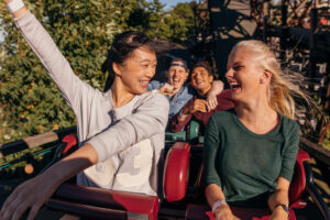 Shot of young friends enjoying and cheering on roller coaster ride. Young people having fun on rollercoaster at amusement park.
