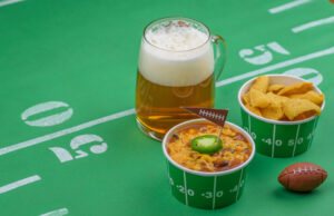 bowl of chili, chips, and beer on table decorated for championship game party