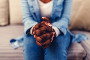 Closeup shot of a woman sitting on couch with her hands clasped at home during the day.