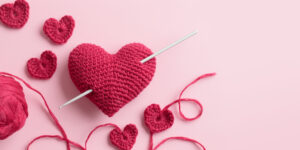 Crocheted amigurumi purple red burgundy hearts with crochet hook on a pink background. Valentine's day banner with a copyspace