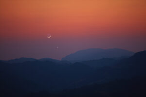 Silhouette of a mountain landscape with Milky Way stars, planets and crescent Moon.