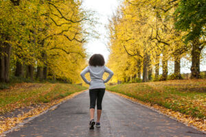 Beautiful mixed race African American young woman girl teenager preparing for fitness running jogging on road of Autumn Fall trees