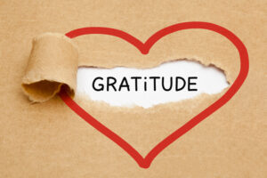 Handwritten word Gratitude appearing behind ripped brown paper.