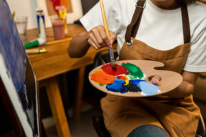 Close up woman hand artist in the darkroom warm light working on painting with brush and variant acrylic color. Female artist painter on canvas in creative studio as art concept