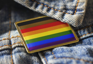 Philadelphia people of color inclusive flag pin on a denim jacket for LGBTQ identity, pride, and activism. The intersectional flag design is public domain for all uses.