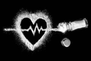 Heart shaped salt with a cardiogram inside with a salt shaker with sprinkled salt. Cardiovascular problems concept. The harm of increased salt intake.