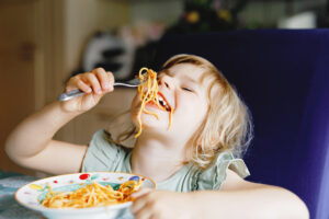 Adorable toddler girl eat pasta spaghetti with tomato bolognese with minced meat. Happy preschool child eating fresh cooked healthy meal with noodles and vegetables at home, indoors