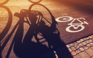 Shadow of unrecognizable cyclist riding a bike on bicycle lane through city street next to the road marking in urban surrounding, retro toned