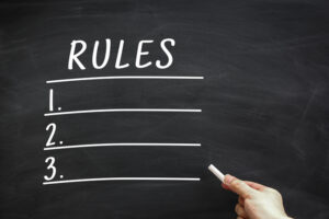 Rules List written on the blackboard with hand holding white chalk aside.